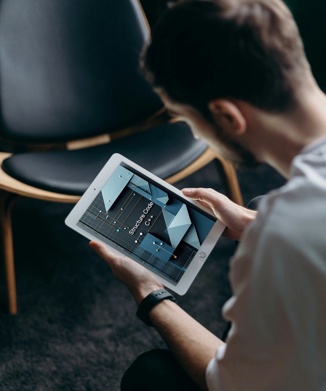 Person using a tablet to learn course "Structure Code" device in a dimly lit room with chairs.